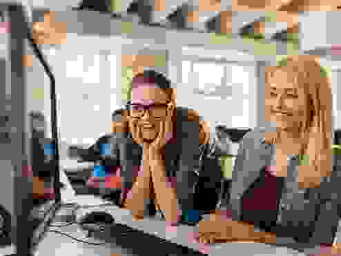 2 girls looking at a screen at workplace and one of them is wearing glasses